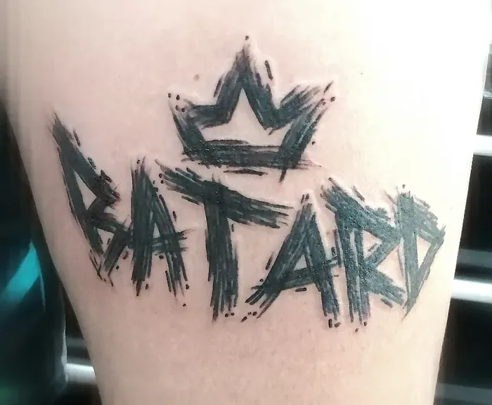 Lettrage graffiti « Bâtard » surmonté de la couronne Bad King, tatoué sur un bras