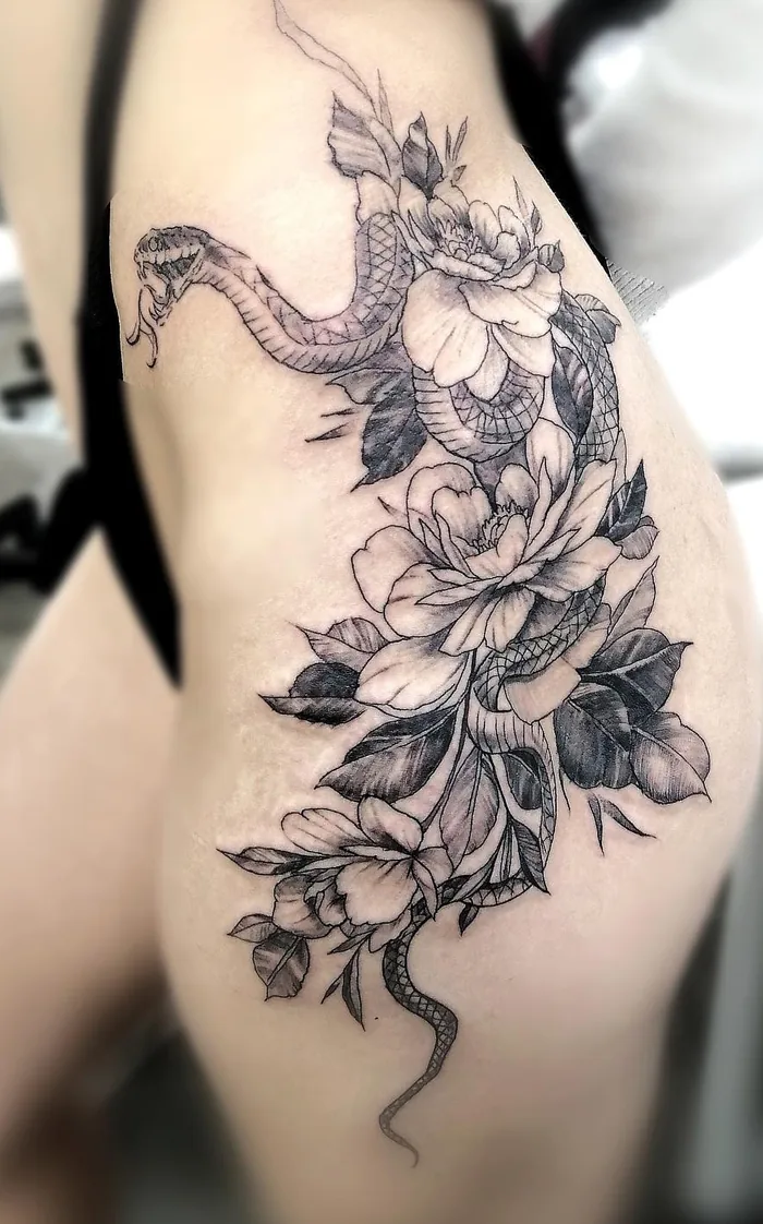 Serpent enroulé dans des pivoines, en noir et gris finement ombré, tatoué sur une hanche